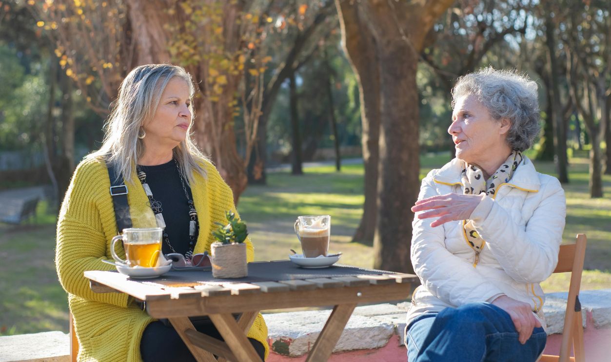 Two senior women enjoying tea and conversation at a park in Portugal
