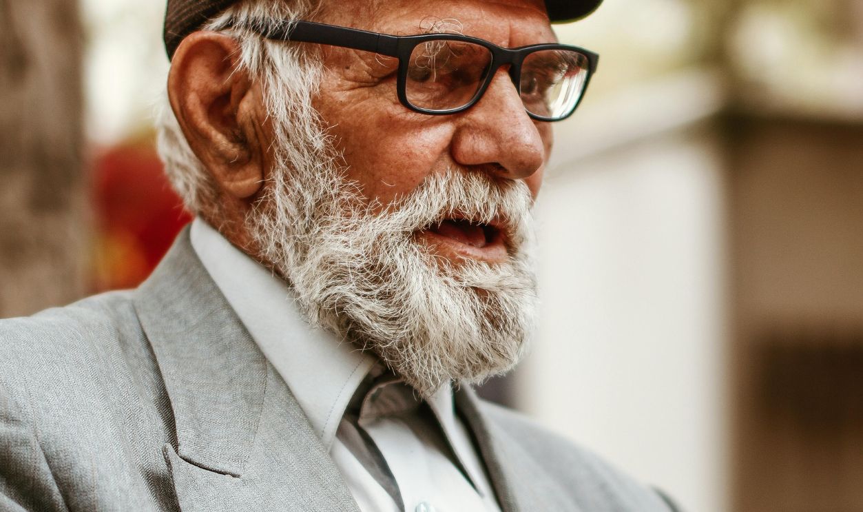 Senior man with beard and glasses wearing a vintage three piece suit outdoors