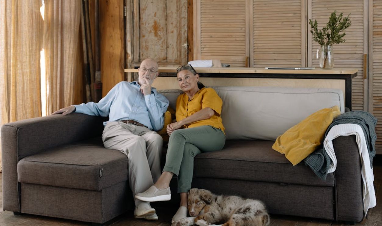 Charming scene of an elderly couple enjoying a cozy moment with their dog on a sofa in a rustic home.