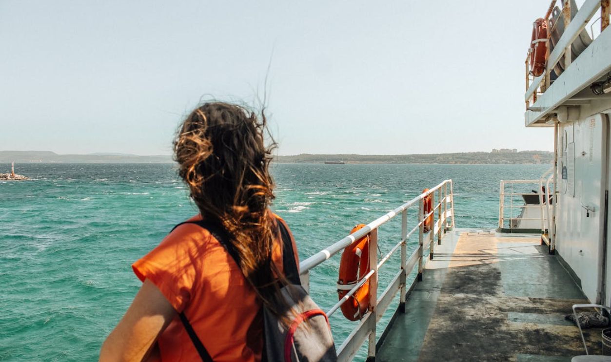 A brunette woman stands on a ferry deck enjoying the ocean view. Perfect for travel and leisure themes.