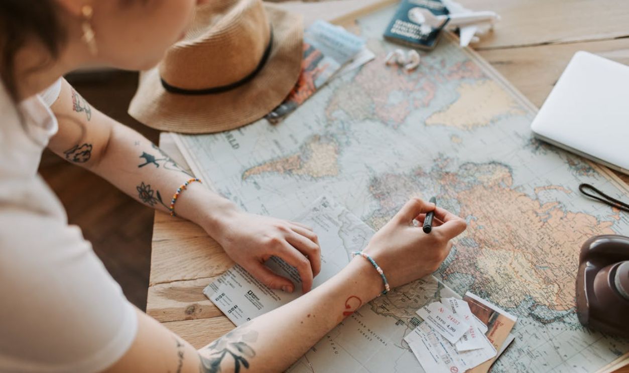 Person planning a journey with a map, passport, and travel essentials on a wooden table.