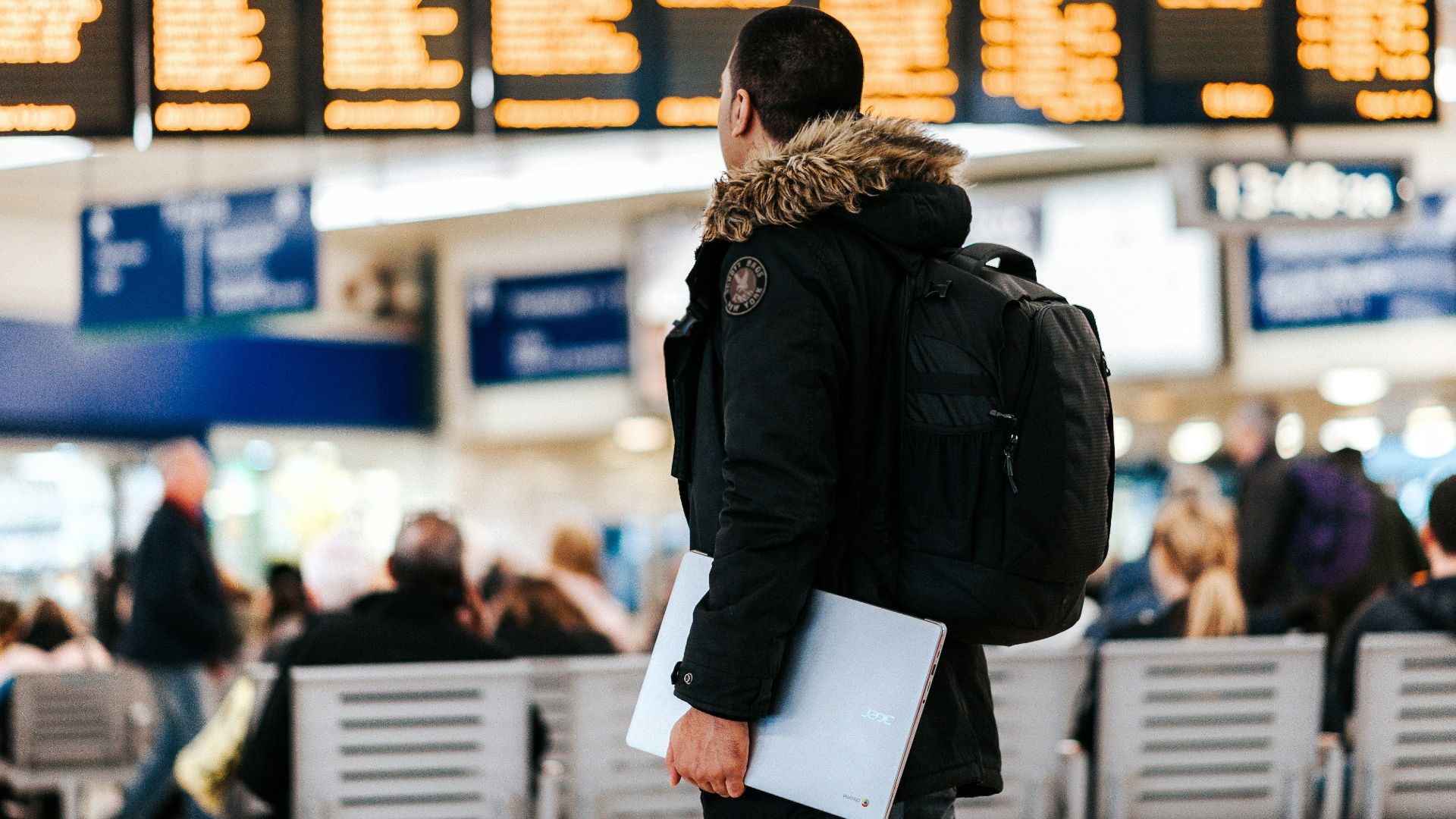 man standing inside airport looking at LED flight schedule bulletin board