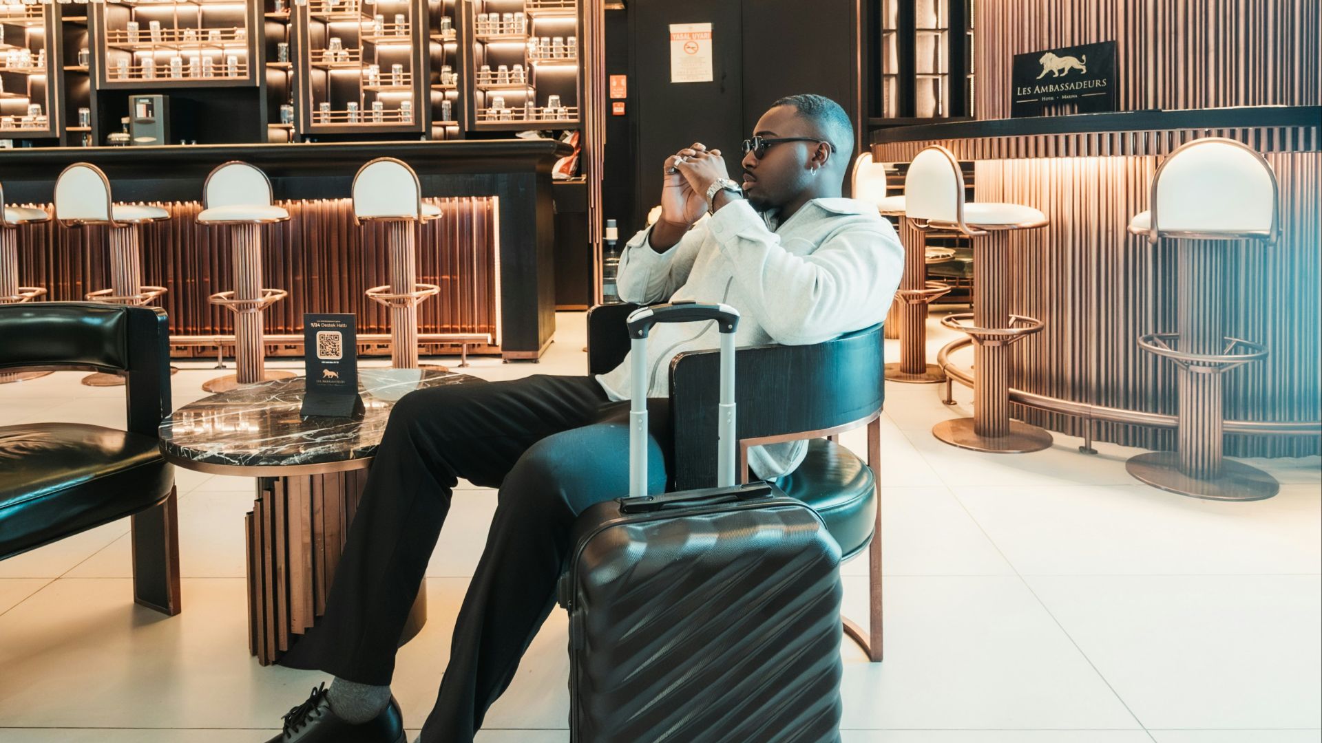 Man sitting with suitcase in stylish hotel lobby.
