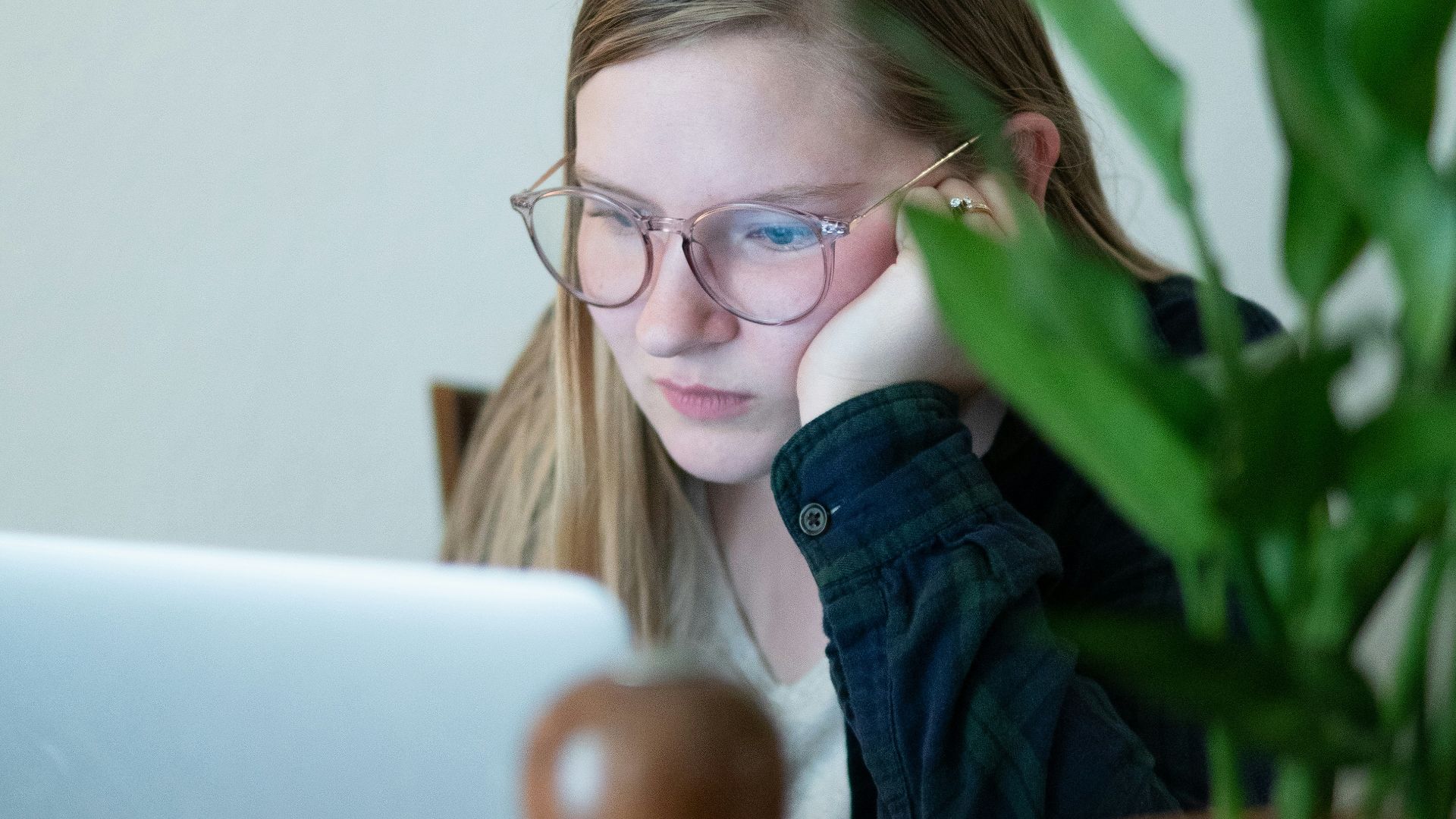 woman in blue denim jacket wearing eyeglasses sitting beside table with macbook
