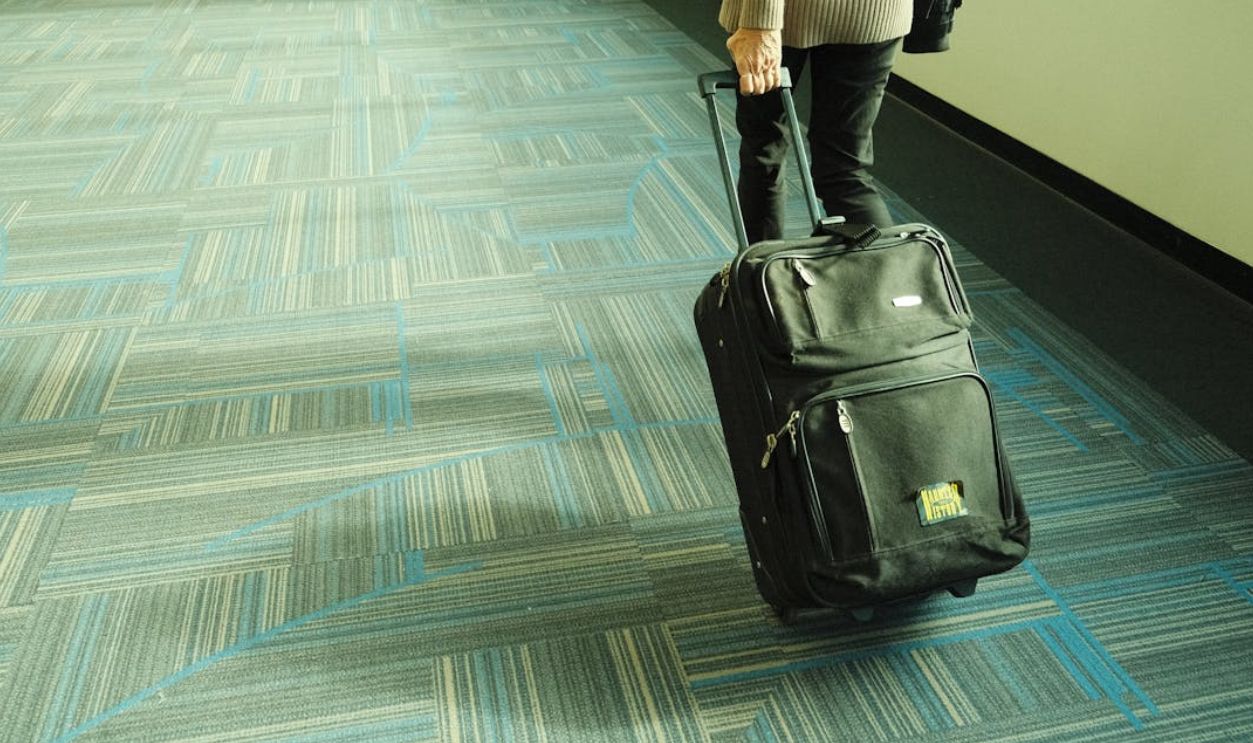 Person walking with luggage on blue carpeted airport corridor, traveling