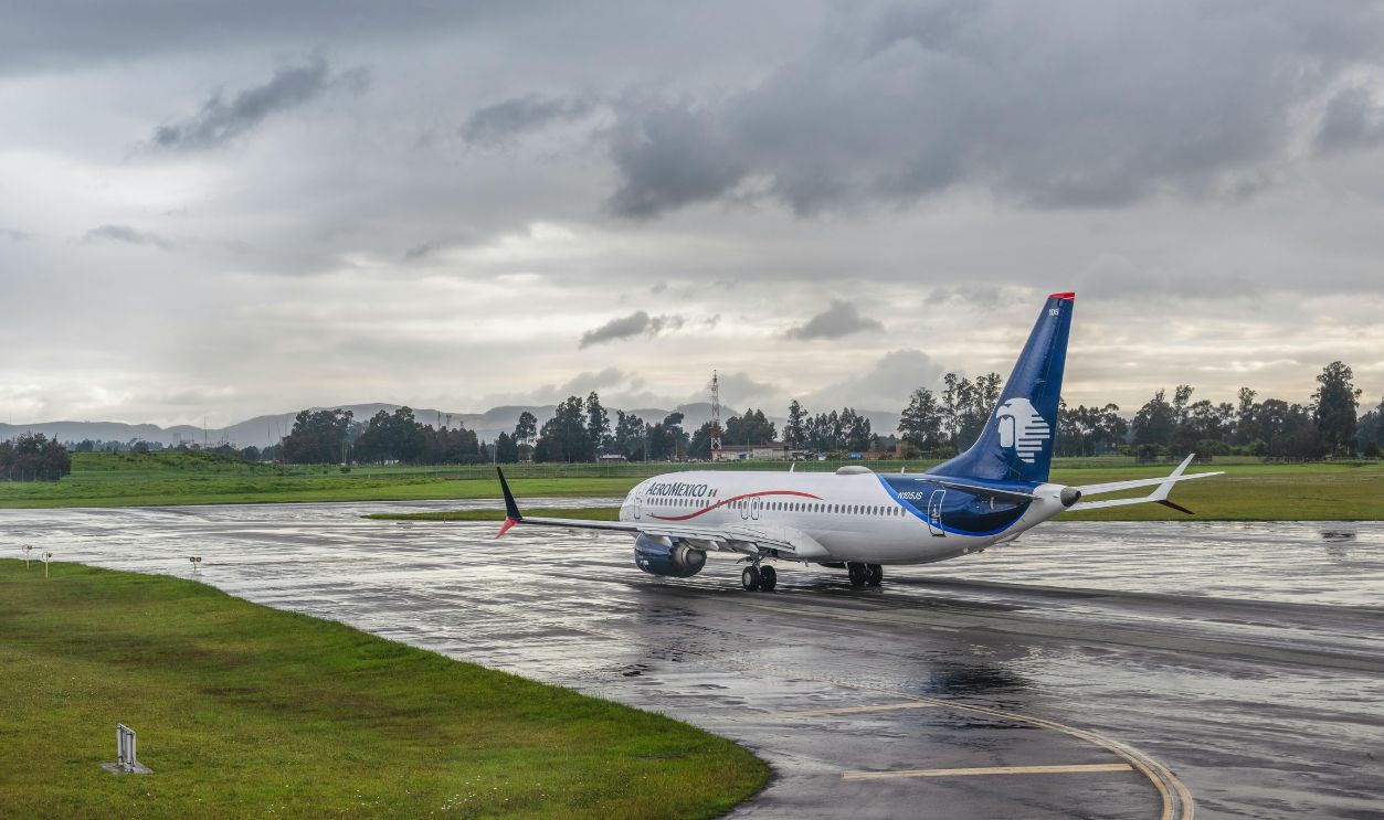 A commercial airplane taxiing on a wet runway under a cloudy sky at an airport