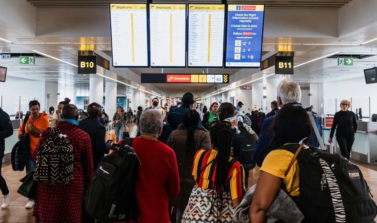 Travelers lining up in a busy airport terminal with baggage under flight information screens