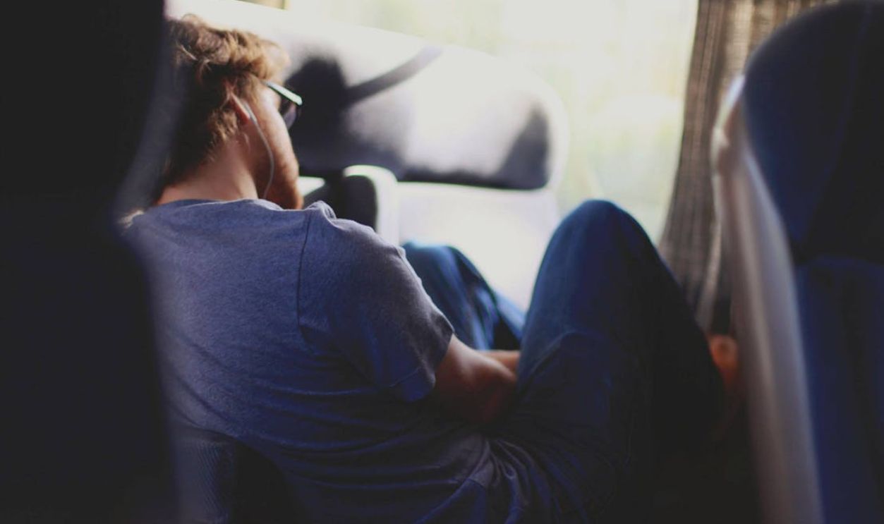 A man comfortably resting on a train seat, enjoying the journey with earbuds