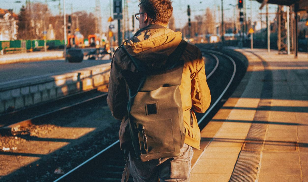 A man with a backpack walks along a train platform, capturing a journey moment in urban daylight