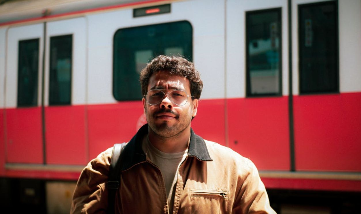 A man with curly hair and mustache stands confidently in front of a train