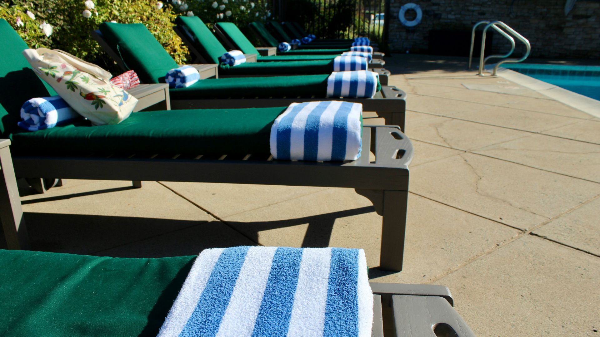 Green lounge chairs with blue striped towels by pool