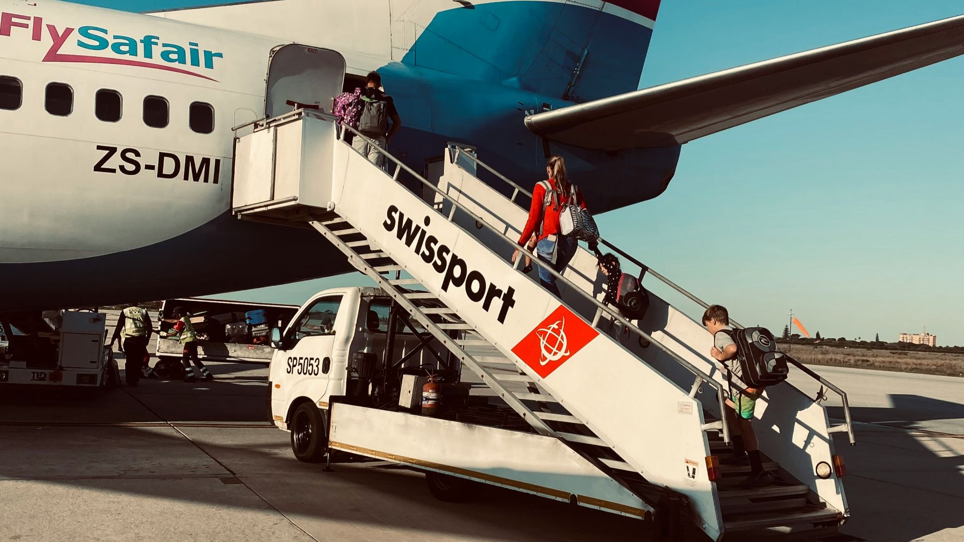 Passengers boarding a flysafair airplane on a sunny day.