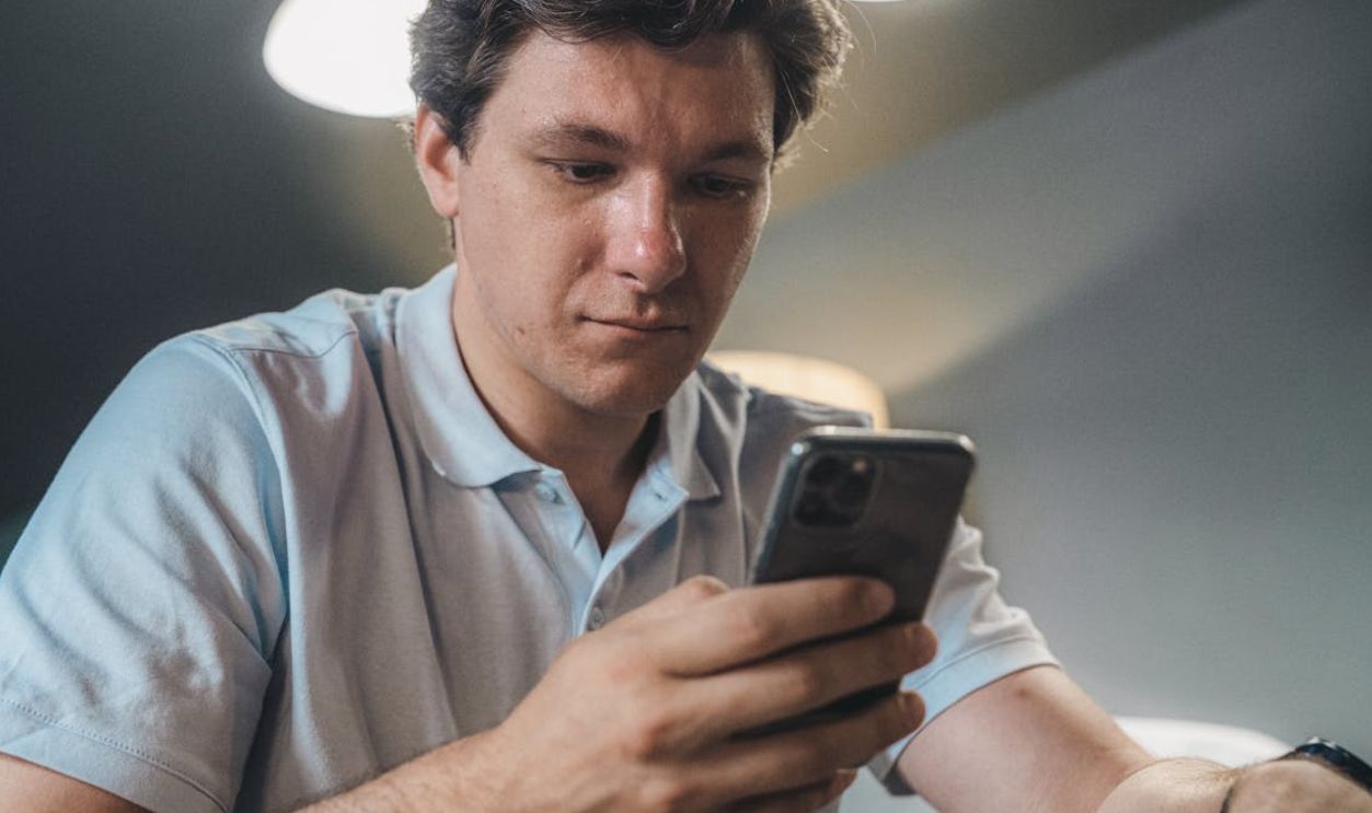 Adult man in casual attire intently using a smartphone indoors, focused and engaged