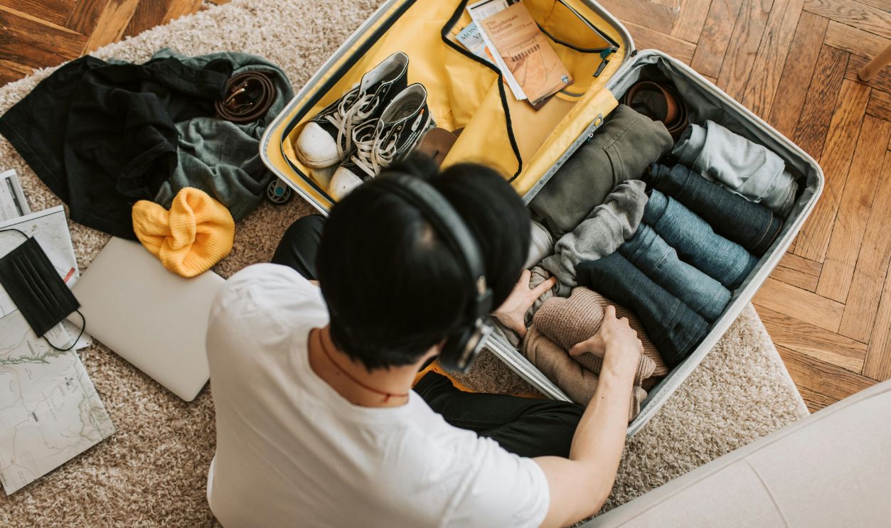 Adult packing clothes in a suitcase while listening to music at home. Overhead view on rug