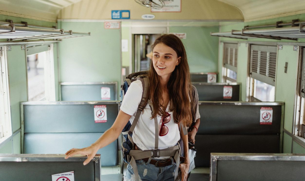 A young woman with a backpack walking inside an empty train cabin