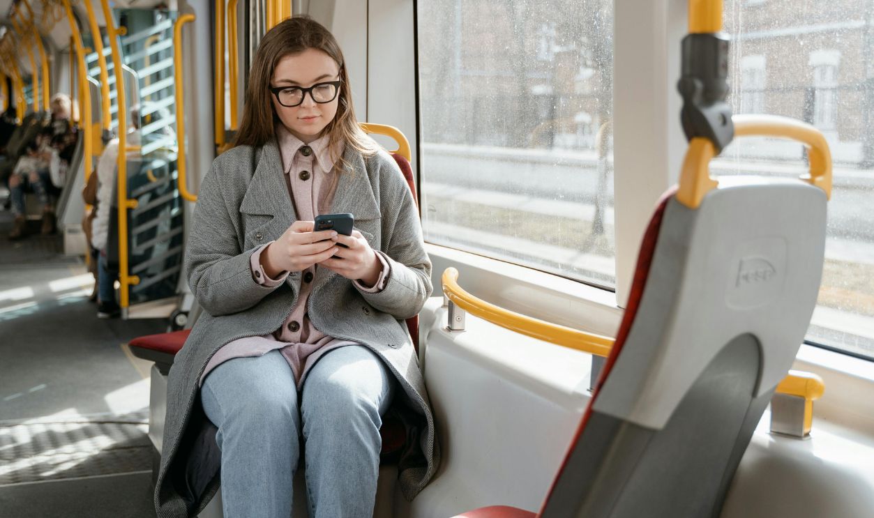 Caucasian woman using smartphone on a tram, wearing a gray coat