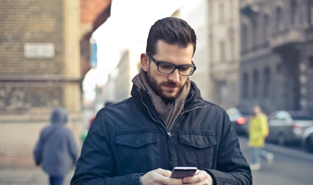 Adult man with glasses using a smartphone on a city street in Budapest, Hungary