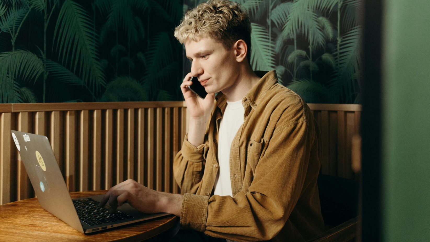 A young man working on a laptop while talking on the phone in a stylish cafe