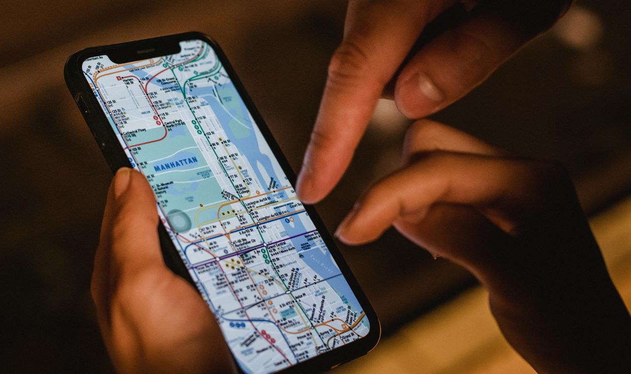 Close-up of hands using a smartphone with a New York City subway map at night, highlighting modern navigation