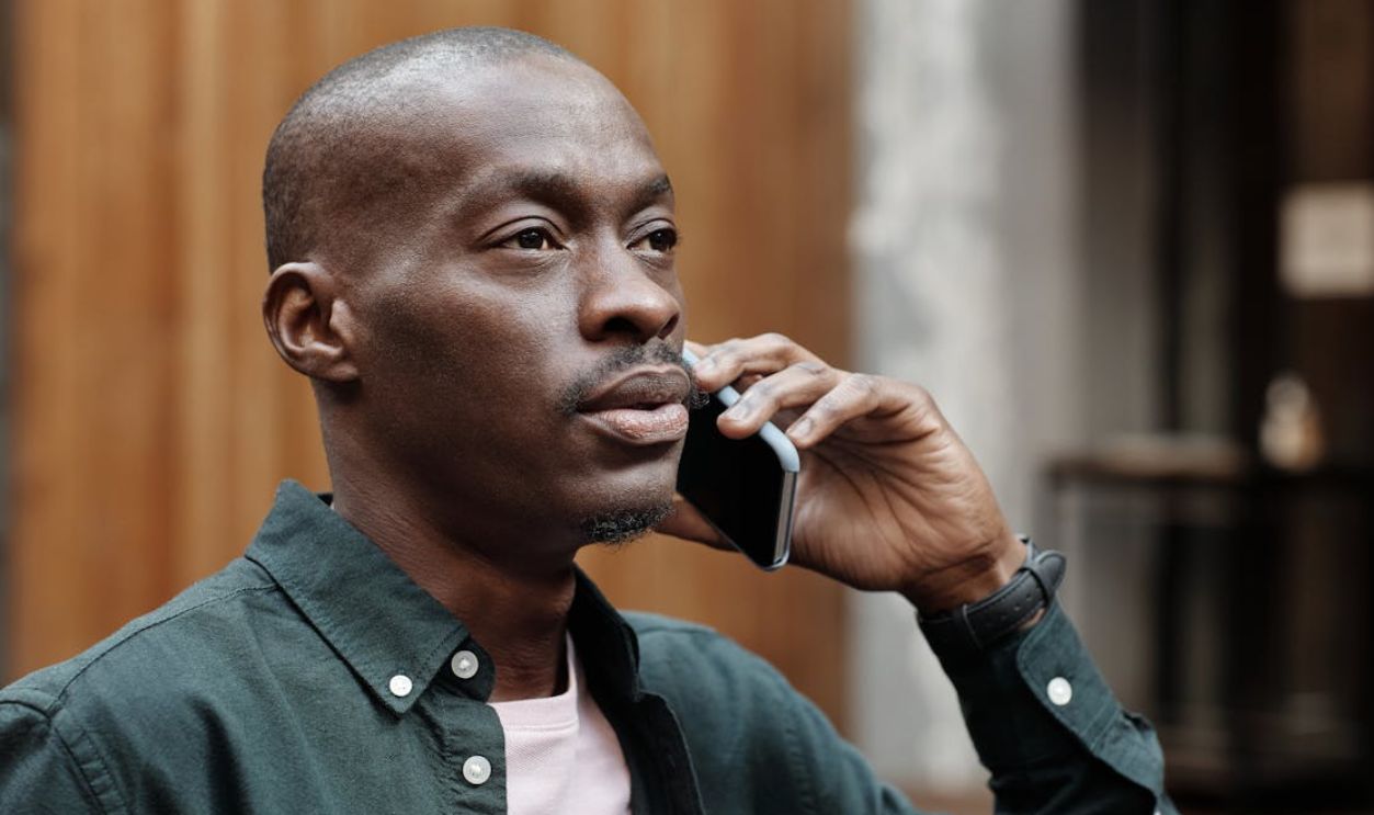 A stylish African American man in a shirt conversing on a smartphone outdoors