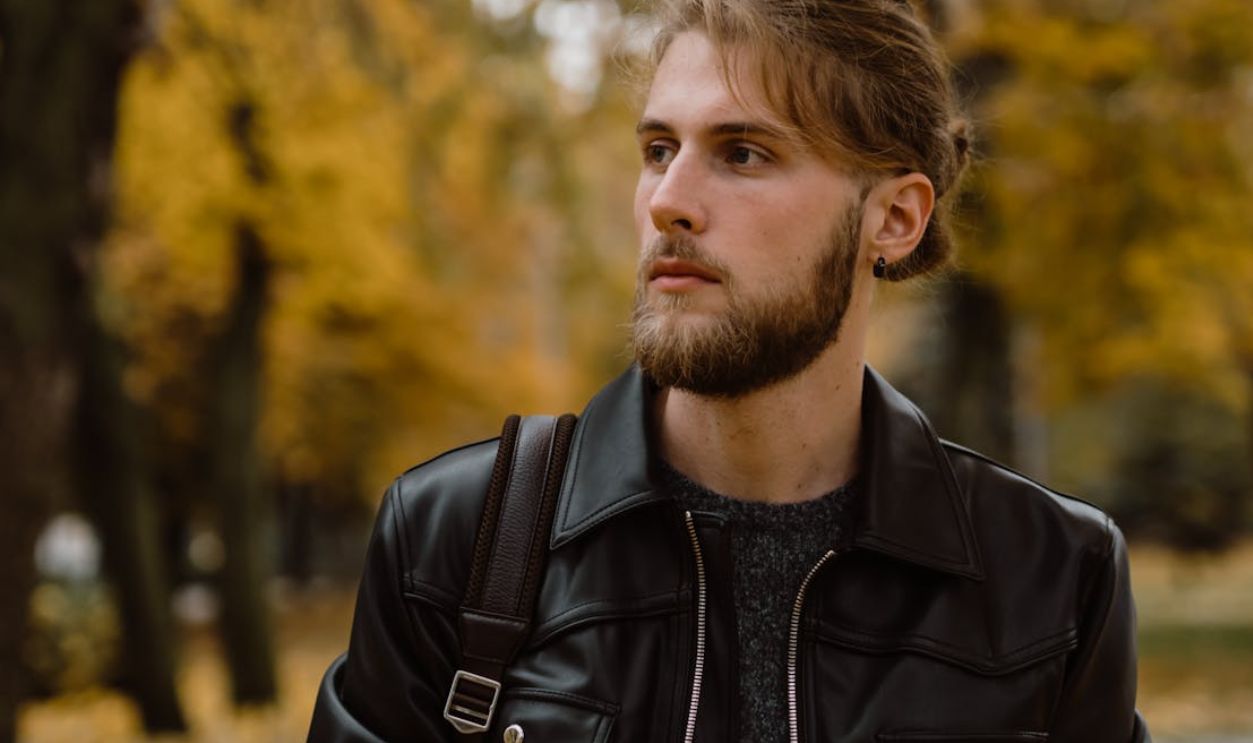 Young man with a beard in a leather jacket outdoors during autumn