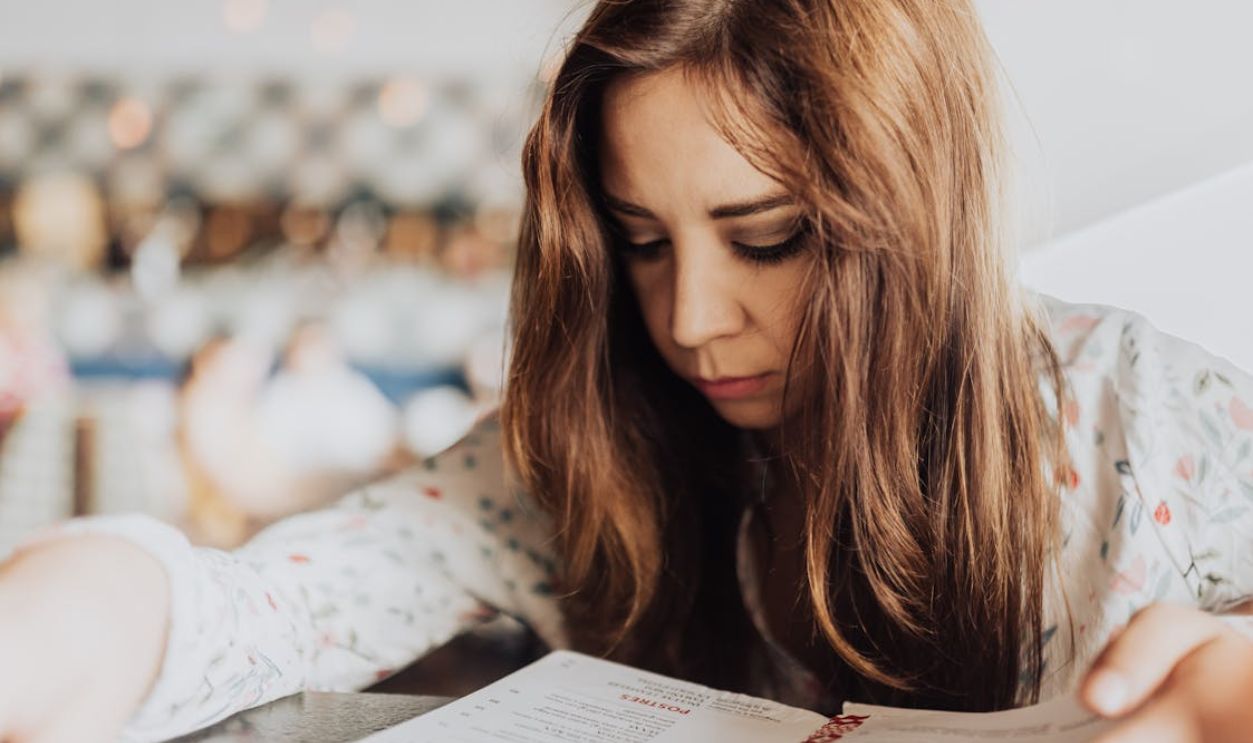 Young woman intensely focused on reading a menu inside a cafe, creating an introspective and cozy atmosphere.