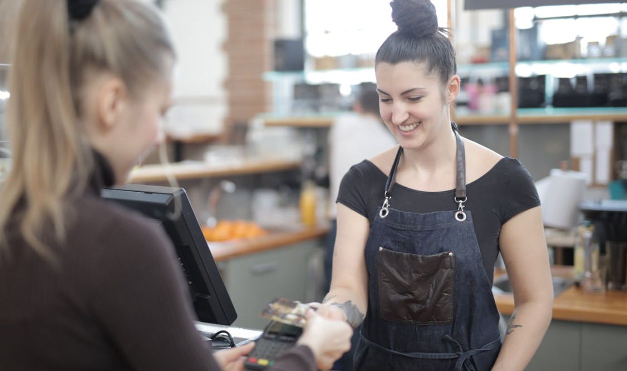 Smiling cashier helping customer with payment at store counter.