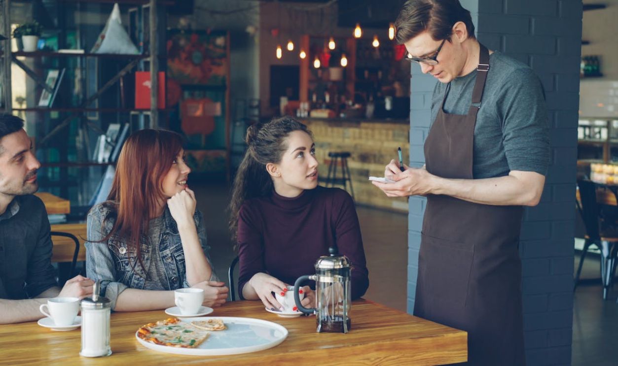 People having a relaxed meeting in a cozy cafe, interacting with a waiter.