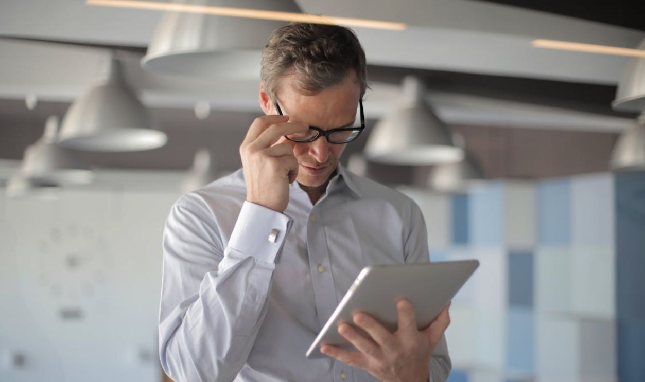 Professional man in eyeglasses focusing on tablet device in a stylish office setting.