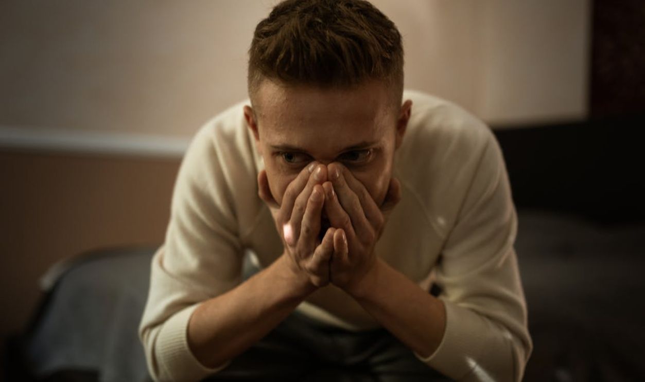 A worried man indoors covering his face with hands, depicting stress or contemplation