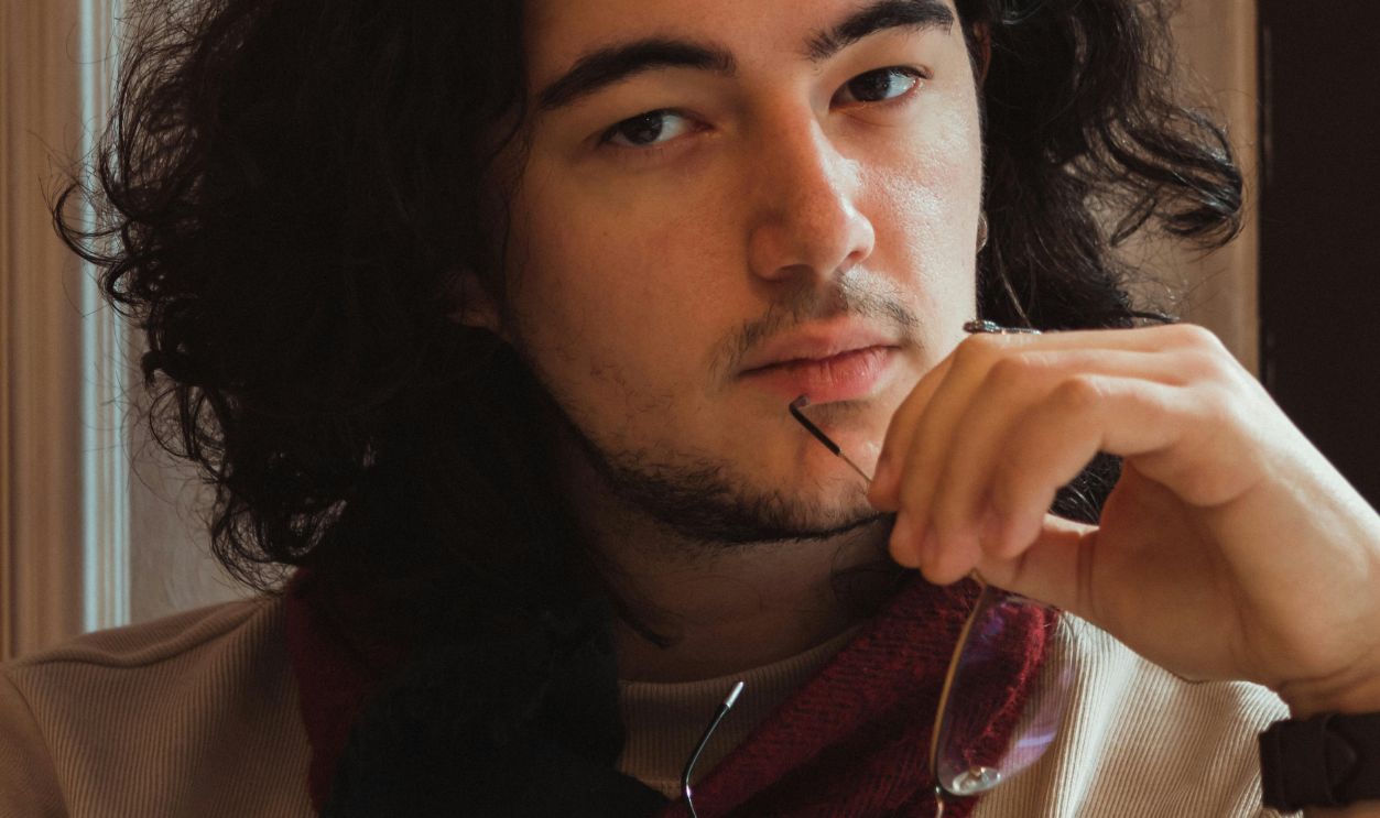 Portrait of a young man with curly hair in casual attire holding eyeglasses thoughtfully