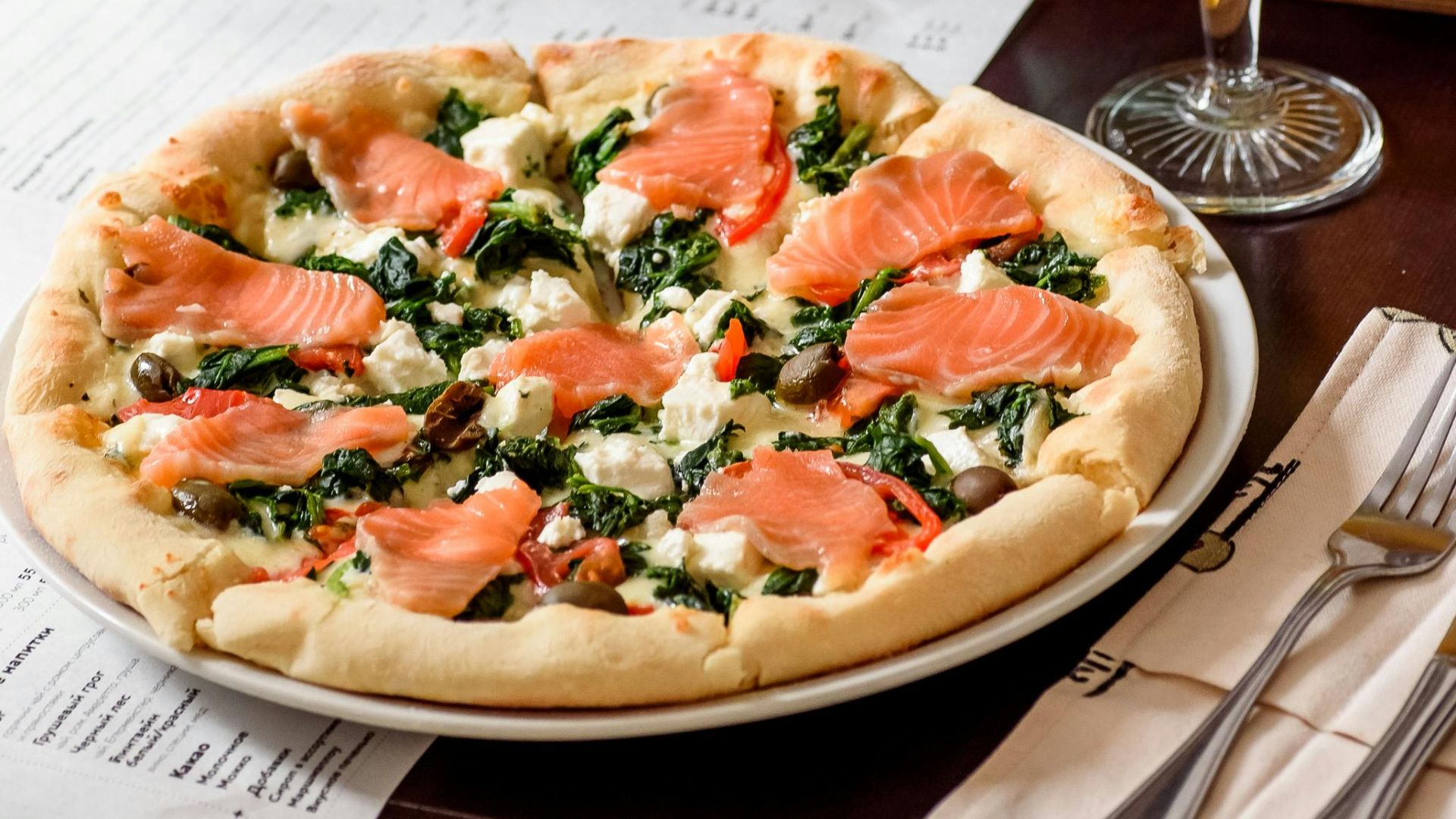 Cozy indoor scene with salmon pizza and a glass of white wine.