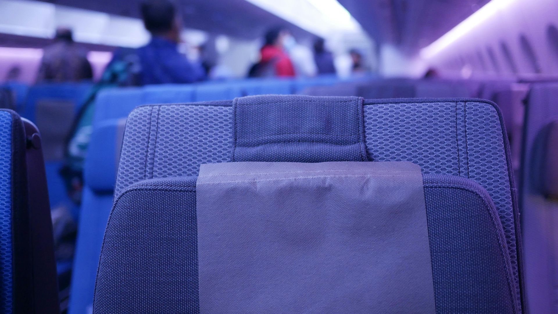 Close-up of airplane seat with blurred passengers in cabin interior lighting.