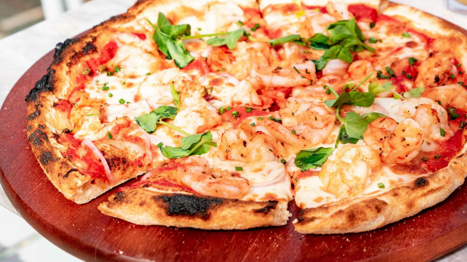 A mouthwatering pizza paired with a glass of beer on a sunny outdoor restaurant table.