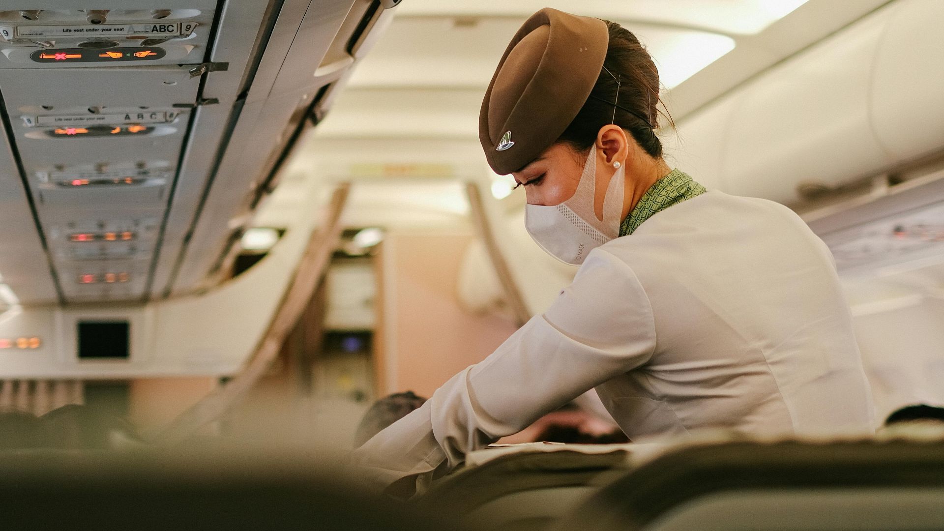 A flight attendant performs duties onboard a passenger airplane while wearing a protective mask.