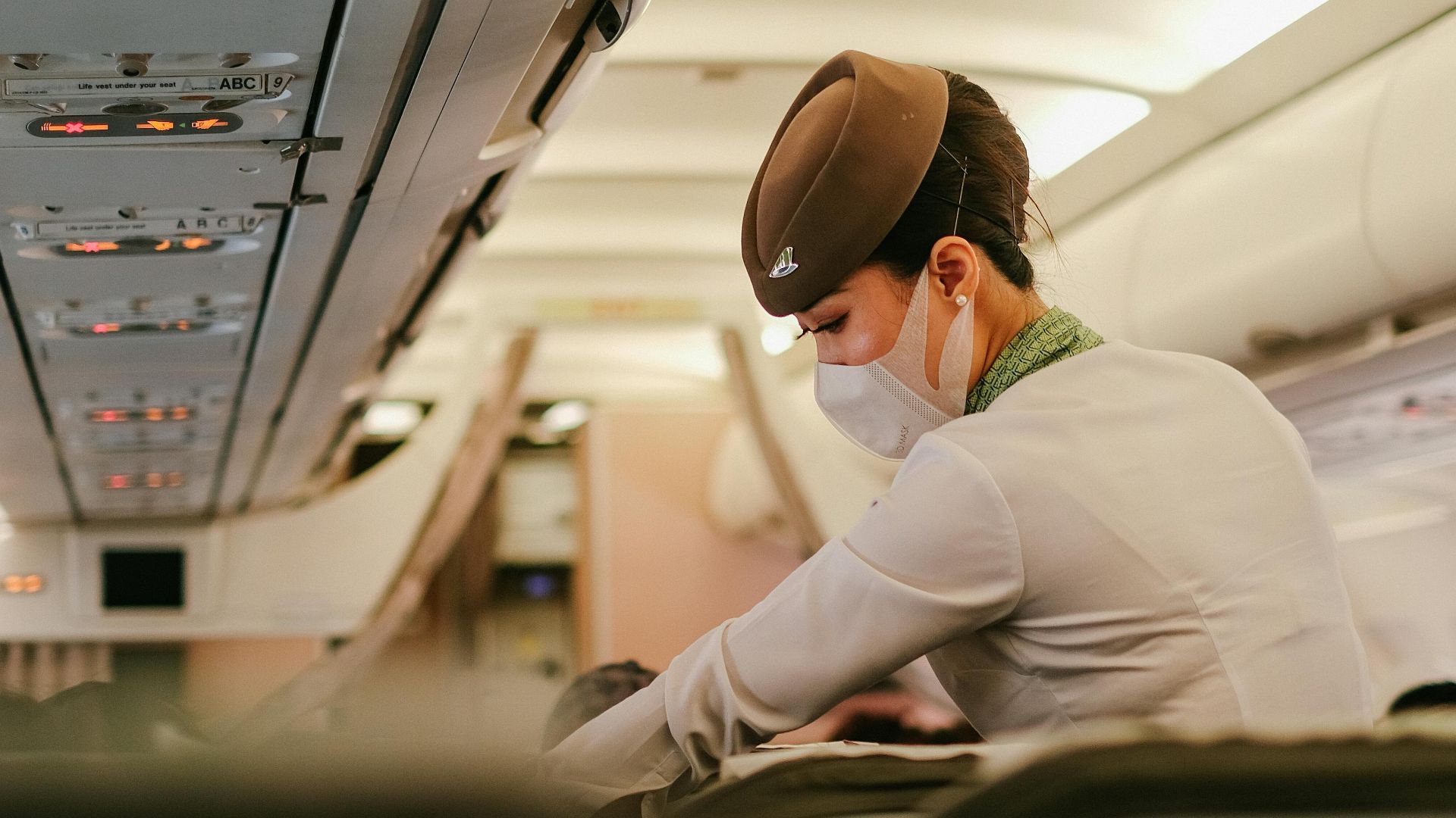 A flight attendant performs duties onboard a passenger airplane while wearing a protective mask.