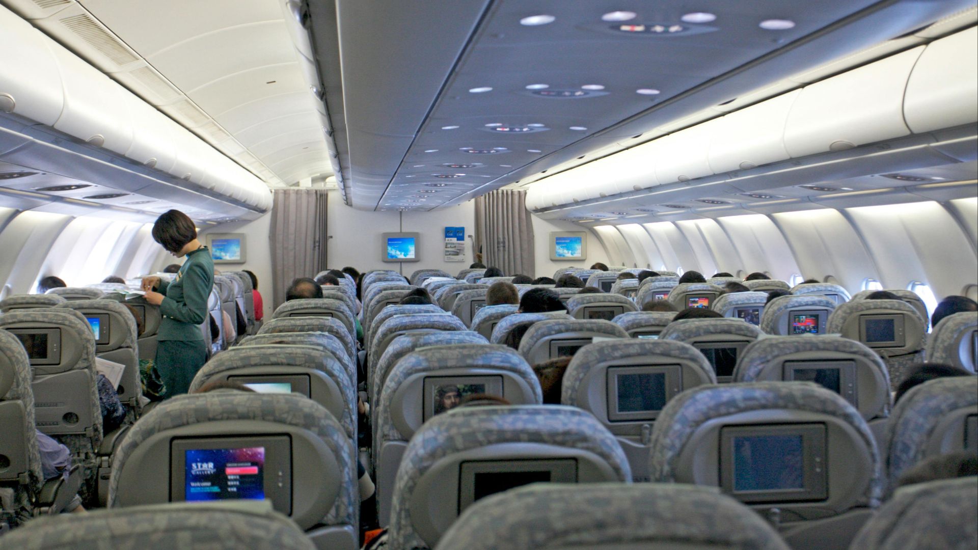 Interior view of a commercial airplane filled with passengers and cabin crew attending to travelers.