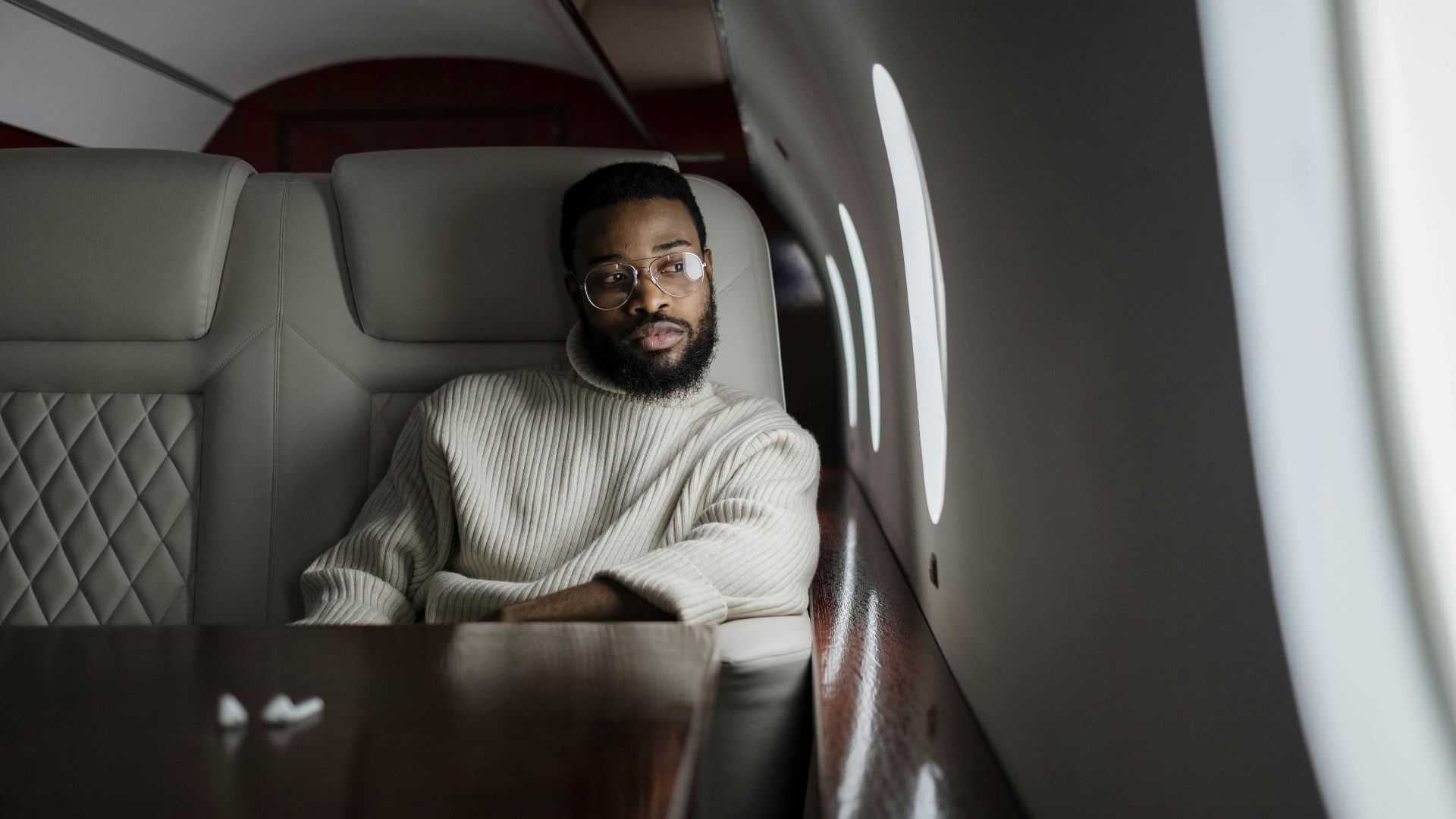 A man in a white sweater relaxes in the luxurious cabin of a private jet during a flight.