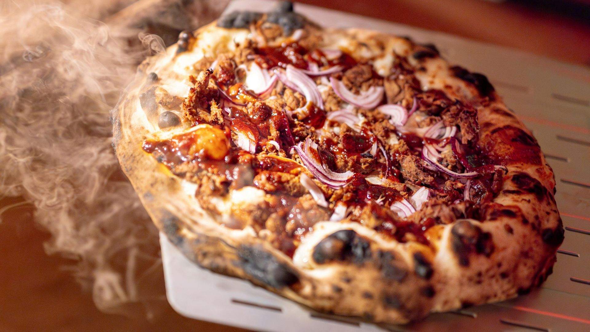 Steaming hot pizza fresh from the oven with melted cheese and onions, captured indoors.