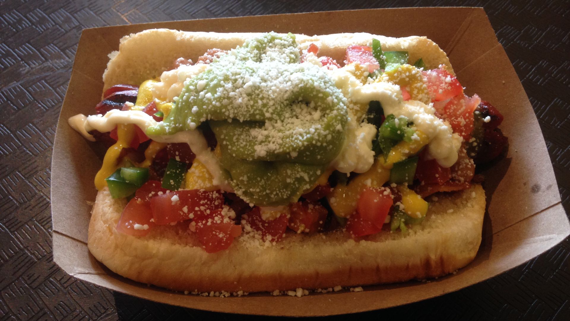 Sonoran hot dog with pinto beans, tomatoes, green salsa, jalapeño, mustard, and mayonnaise, and with avocado and cotija cheese on top. At Ivy's in Chicago.