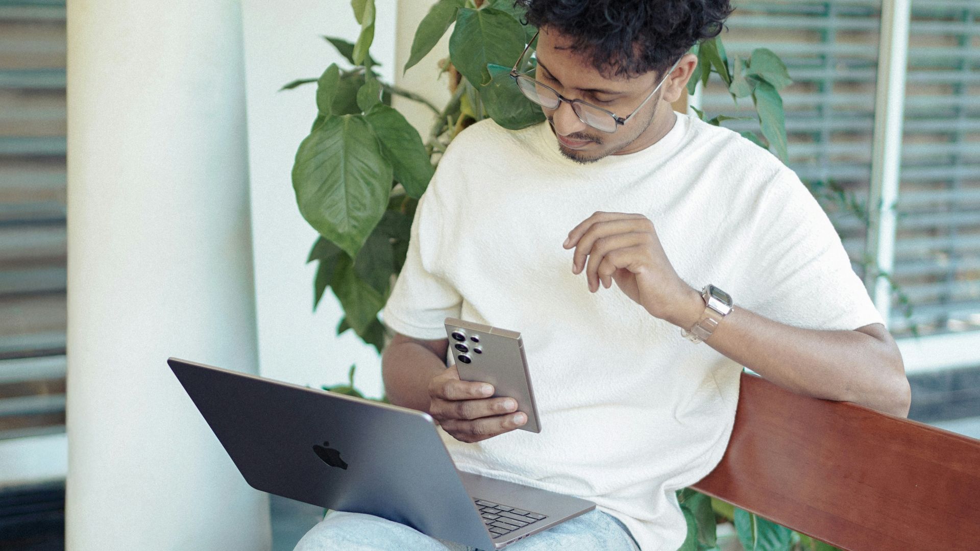 Man is using phone and laptop outdoors.