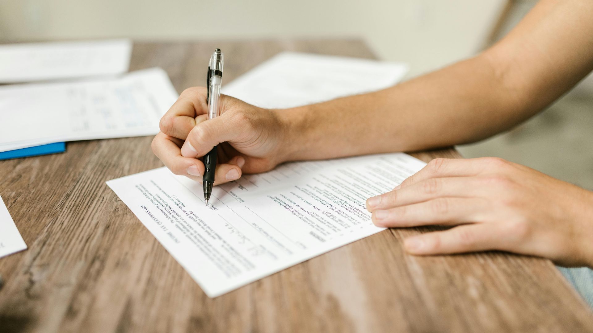 Hand filling out paperwork with a pen, showcasing focus on document completion.