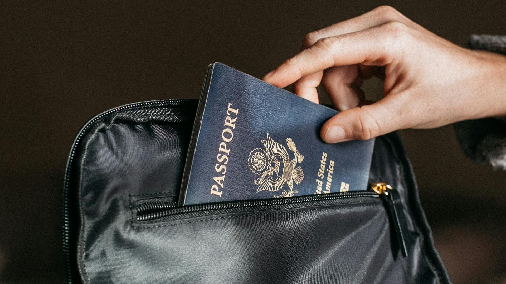Close-up of a person placing a passport into a leather bag, ready for travel.