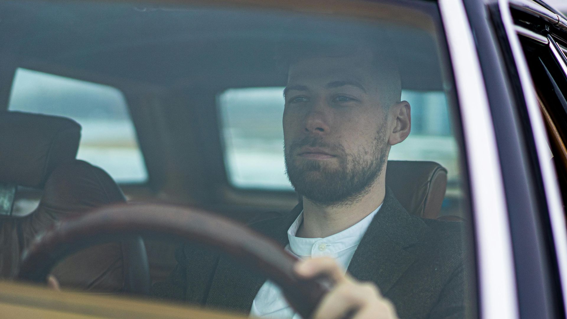 A thoughtful man drives a car, looking focused through the windshield on a cloudy day.