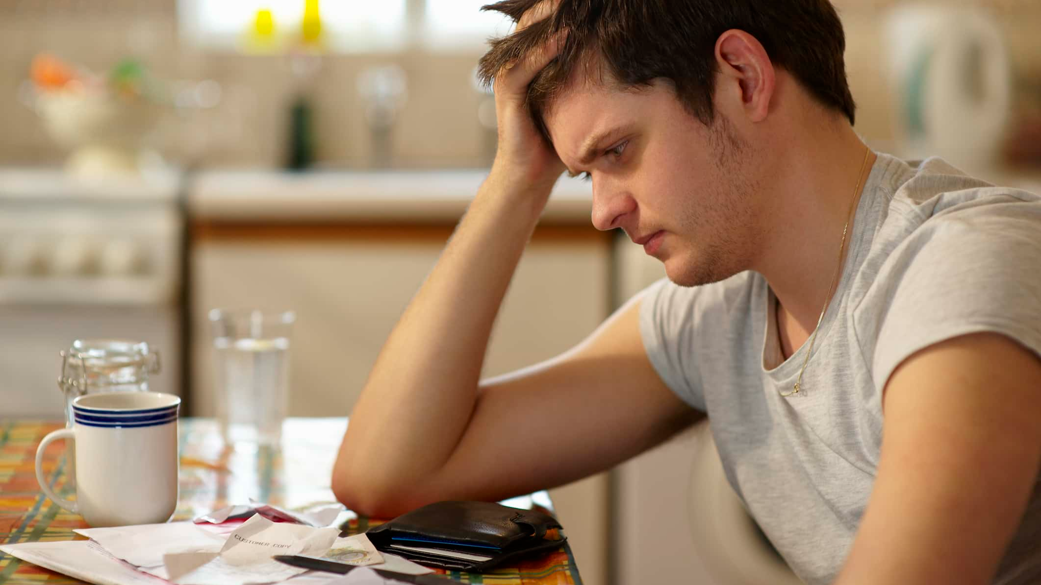 Young man holding head looking at receipts.