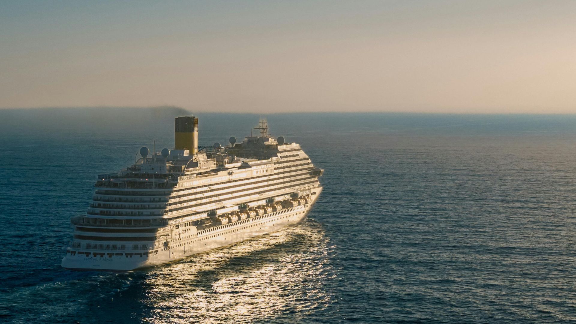 A cruise ship gracefully sails across the ocean at sunset, creating a tranquil scene.