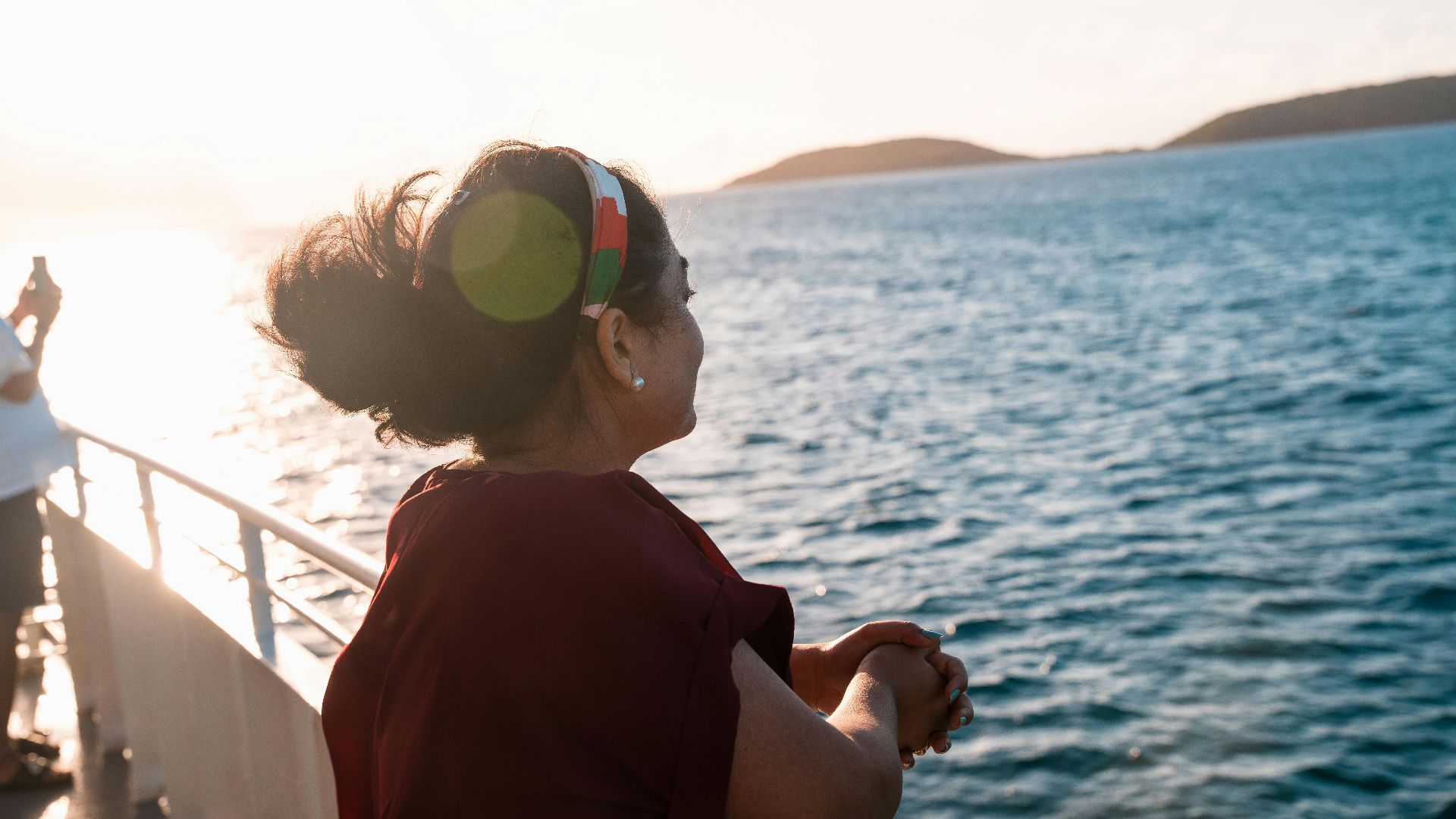 A woman gazes out over the ocean as the sun sets, creating a warm, peaceful ambiance.