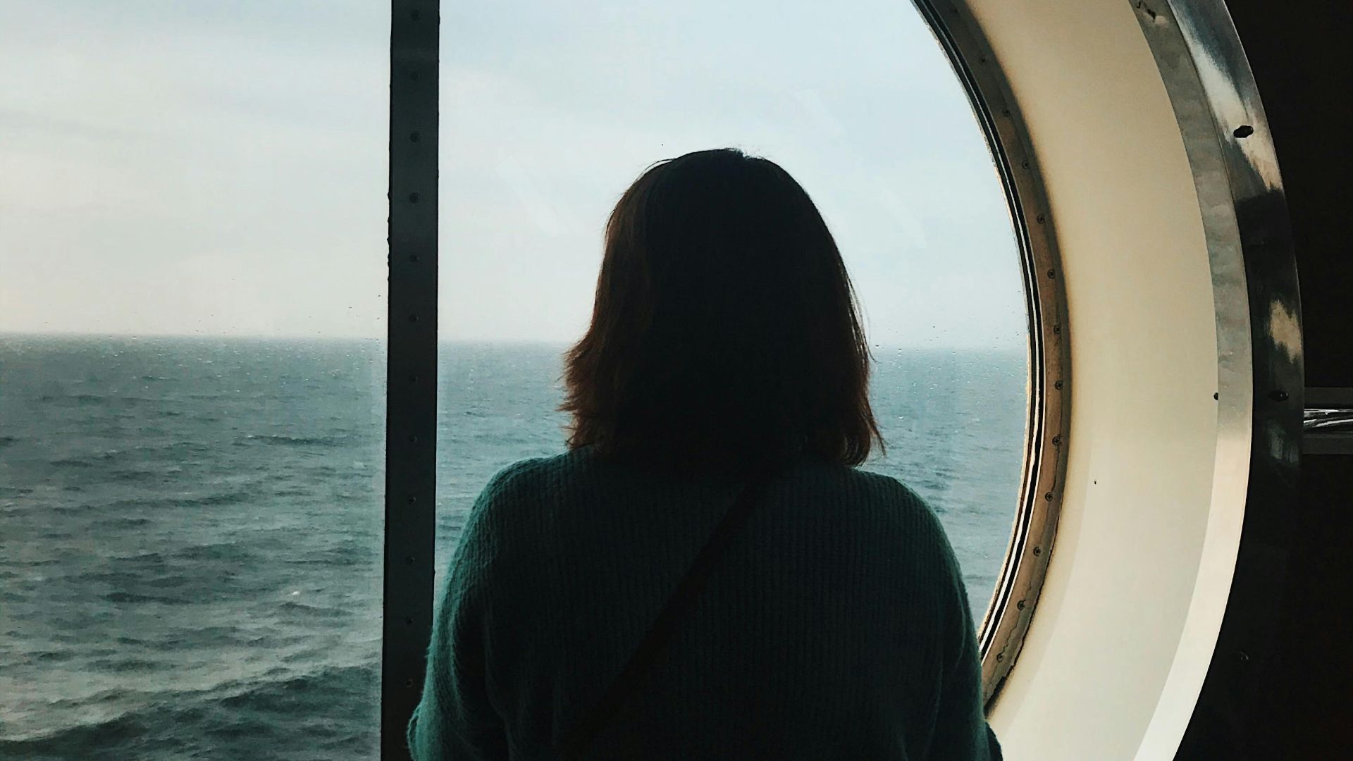 A serene moment of contemplation as a woman views the sea through a porthole window on a cruise ship.