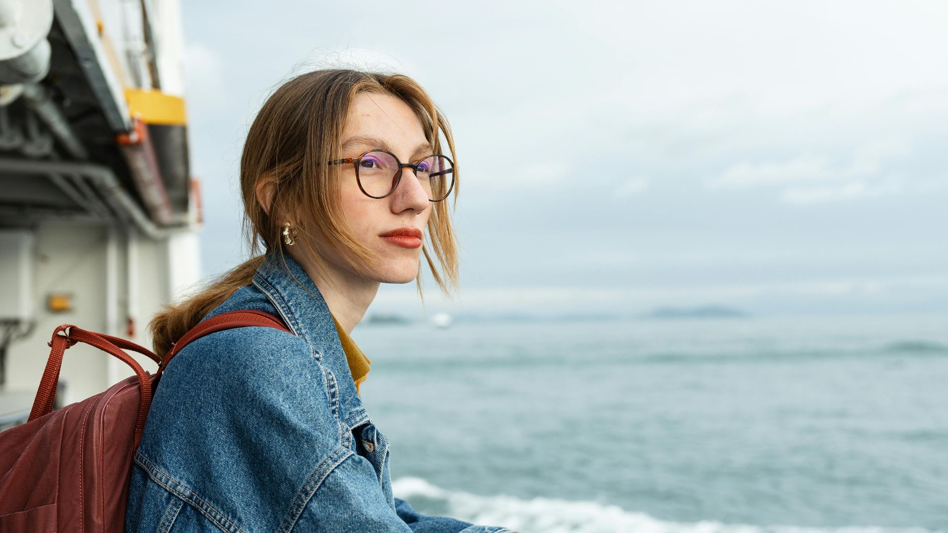 A woman with a backpack gazes at the ocean from a cruise ship deck, capturing a serene moment at sea.
