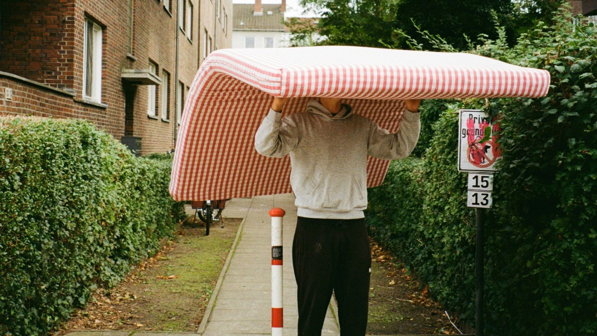 Man carrying a mattress down a sidewalk.